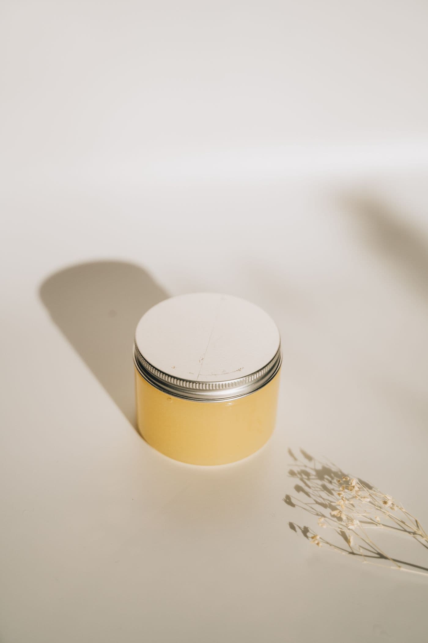 Yellow-tinted jar of Dew Balm with its lid resting beside it on a clean white surface.