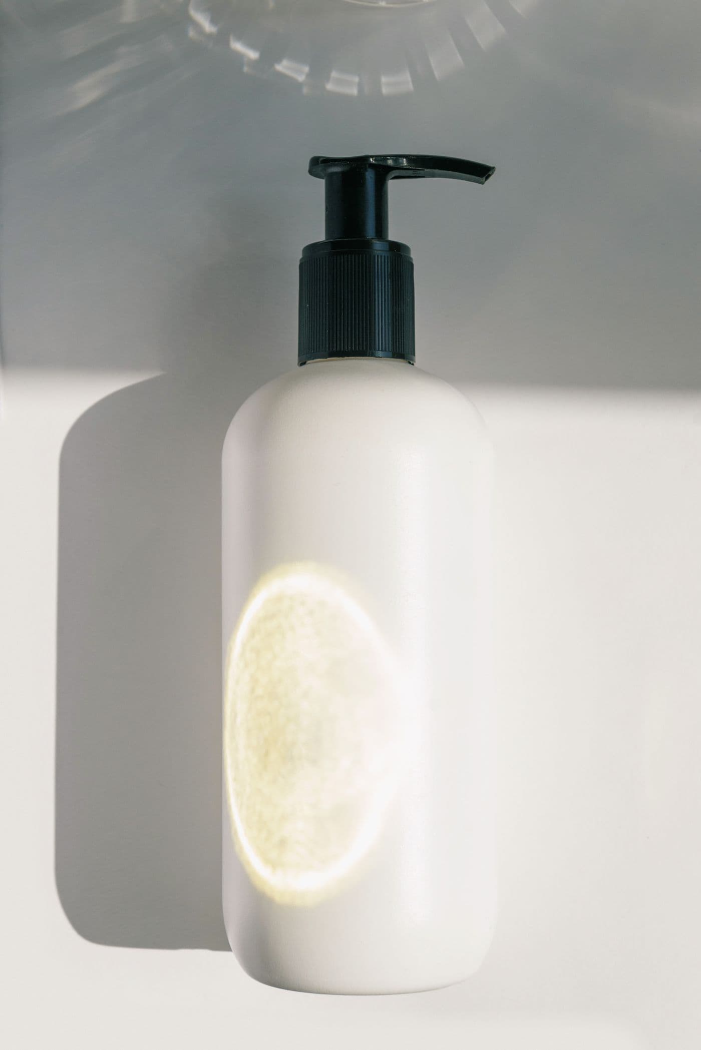 White pump bottle of Clay Wash Shampoo lit by warm sunlight against a plain background.