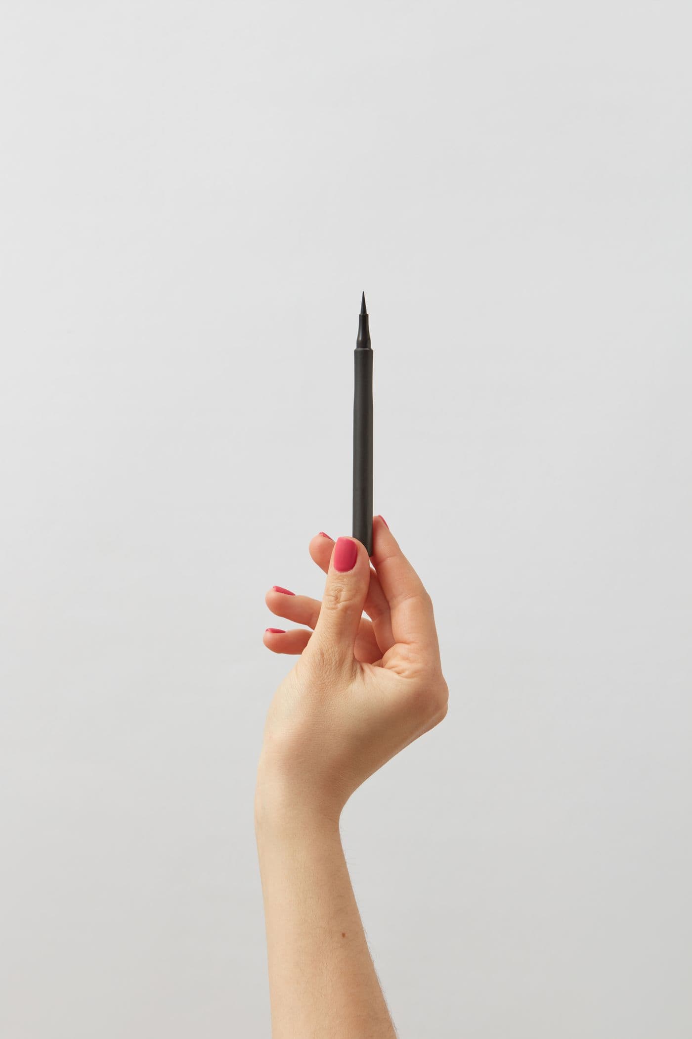 A hand holding the slim black Ink Gel Liner pen against a plain light grey background.