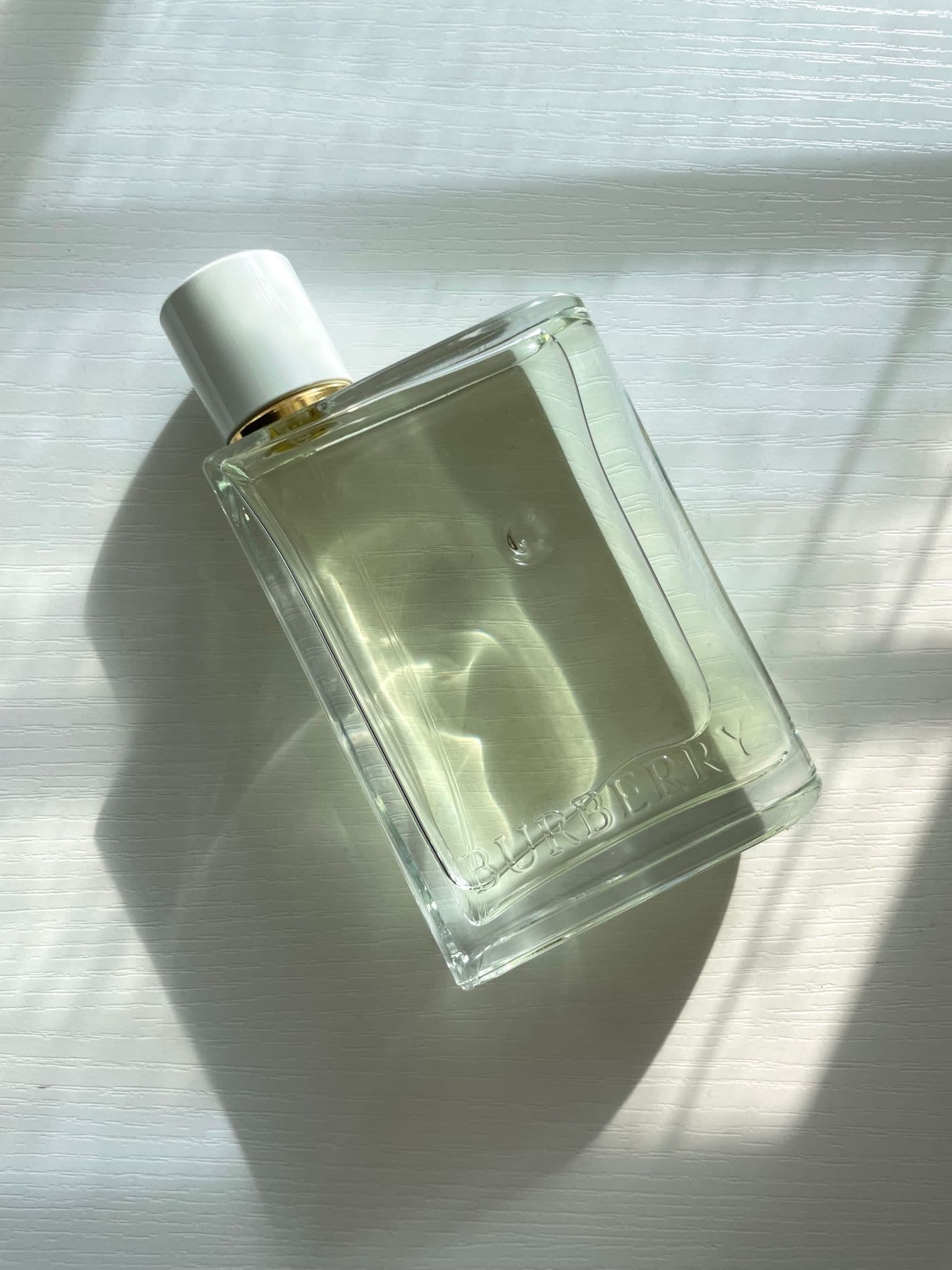 Clear glass bottle of Quiet Bloom Eau de Toilette catching afternoon light and shadow.
