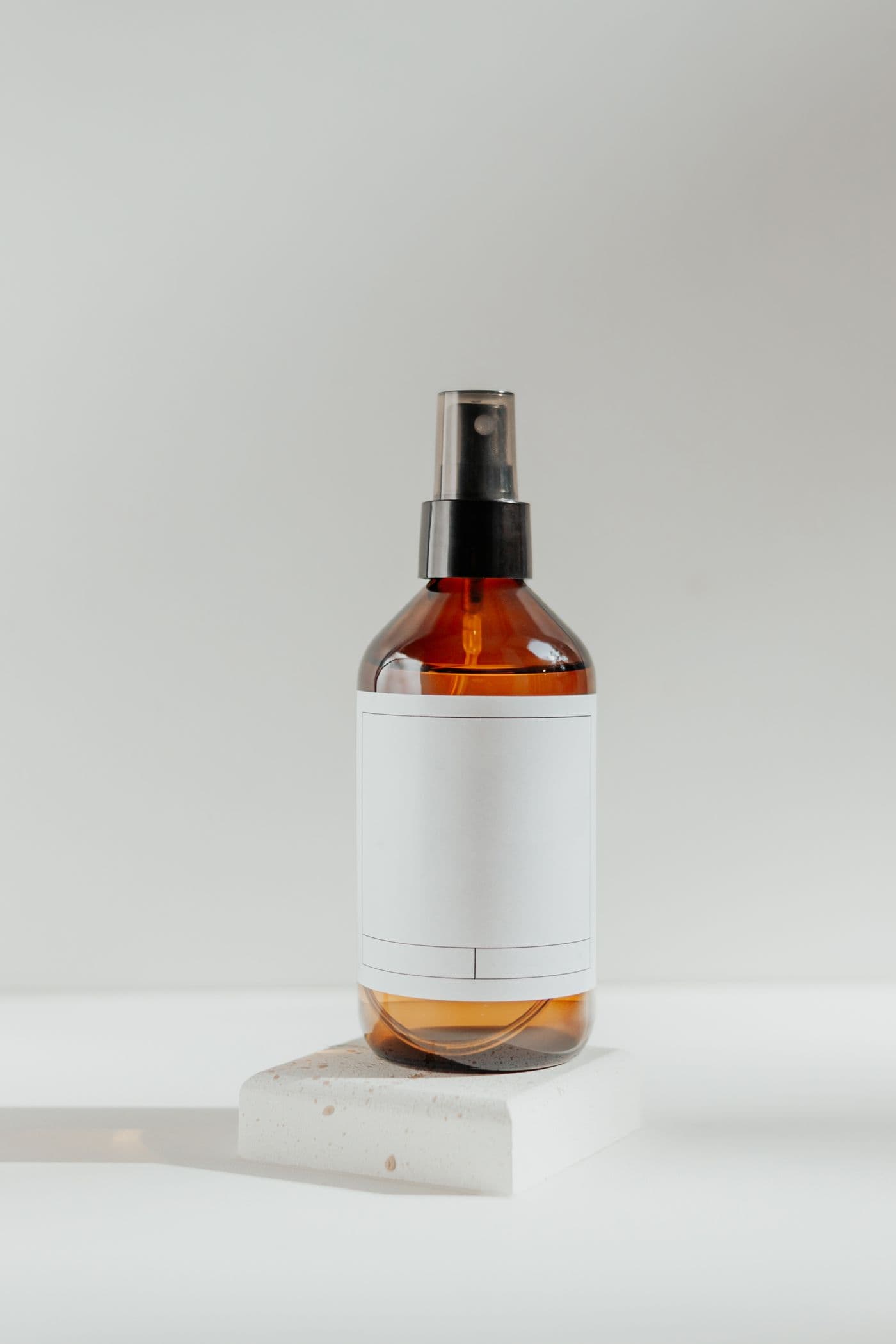 Amber spray bottle of Sage Leave-In Mist with a blank label, standing on a wooden block.